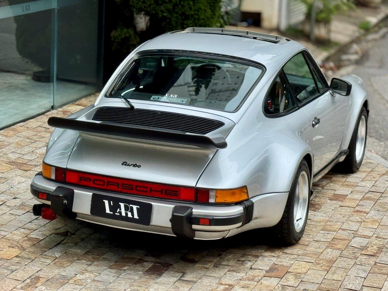 Porsche 930 Turbo 3.0 1975 prata visto de traseira em ângulo, com a grande asa traseira